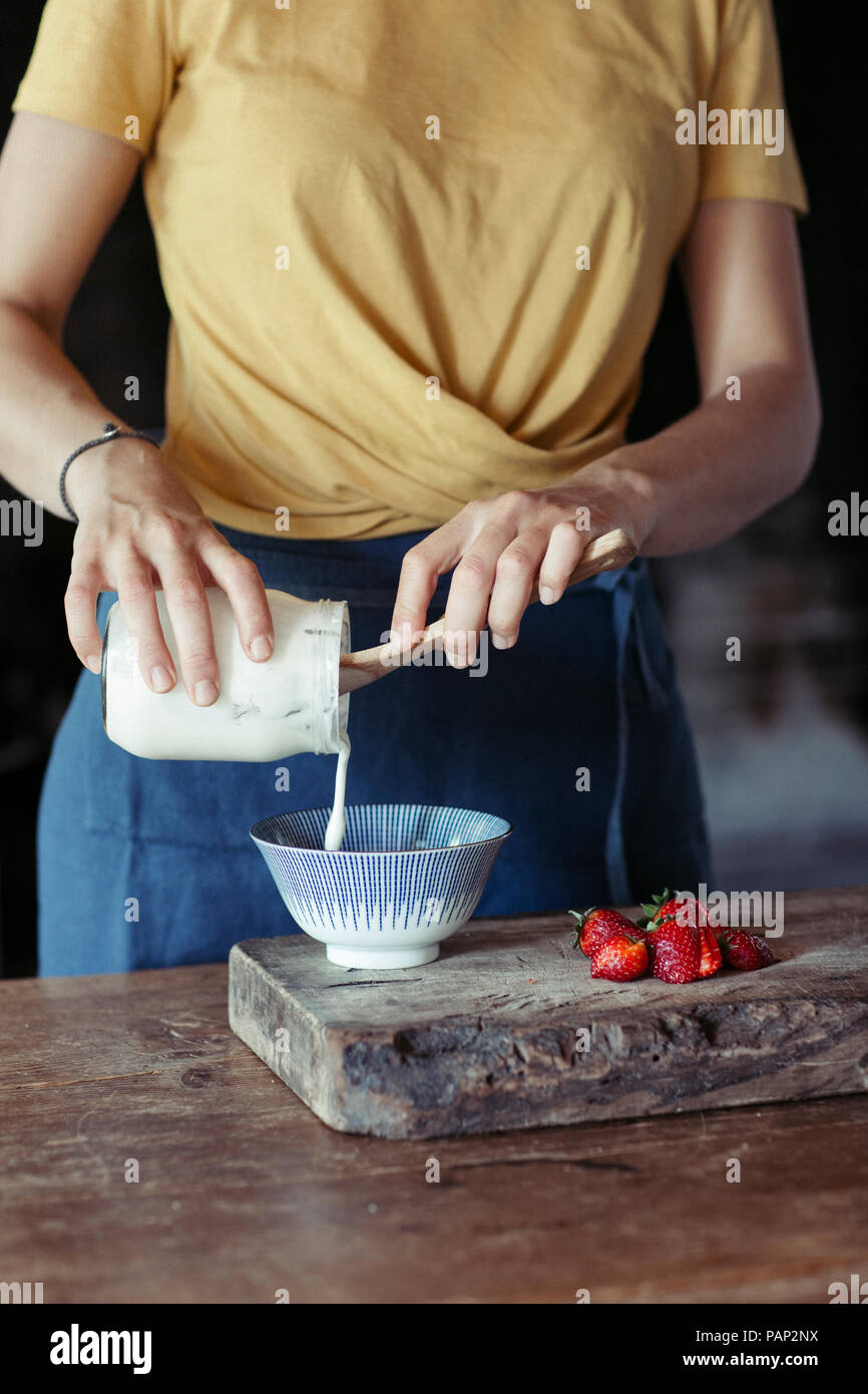 La donna la preparazione di muesli, yogurt versare in una terrina di fragole fresche Foto Stock