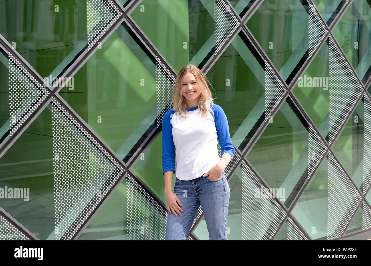 Giovane donna bionda appoggiata su una facciata di vetro Foto Stock