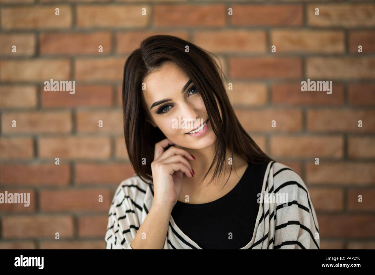 Ritratto di sorridente giovane donna con capelli lunghi marrone di fronte a un muro di mattoni Foto Stock Ritratto di sorridente giovane donna con capelli lunghi marrone di fronte a un muro di mattoni Foto Stock