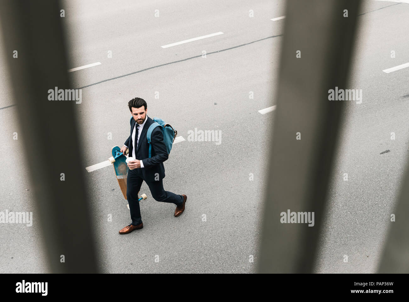 Imprenditore con caffè da asporto e skateboard a camminare sulla strada Foto Stock