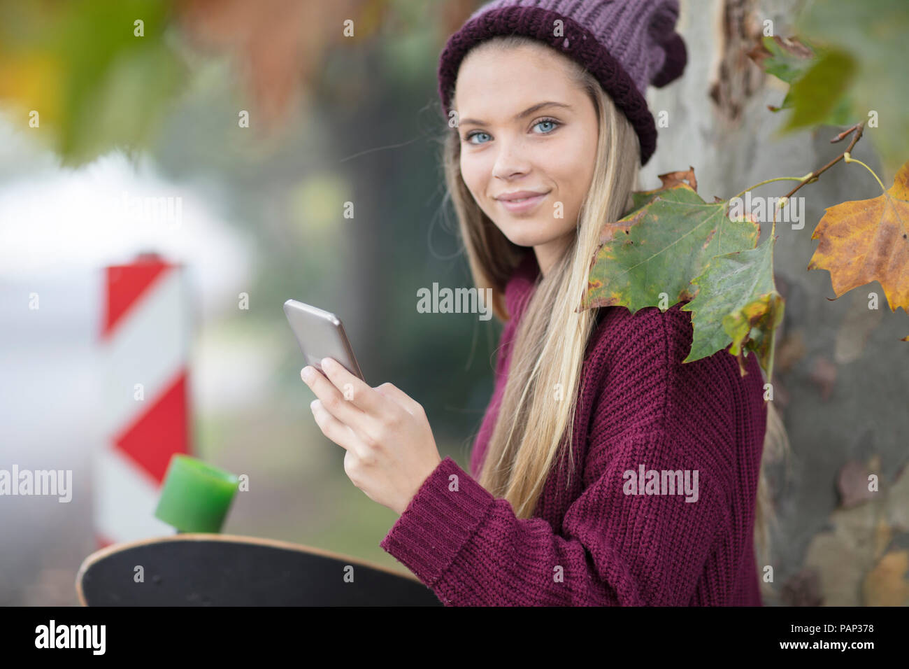 Ritratto di sorridente ragazza adolescente con un telefono cellulare e lo skateboard Foto Stock