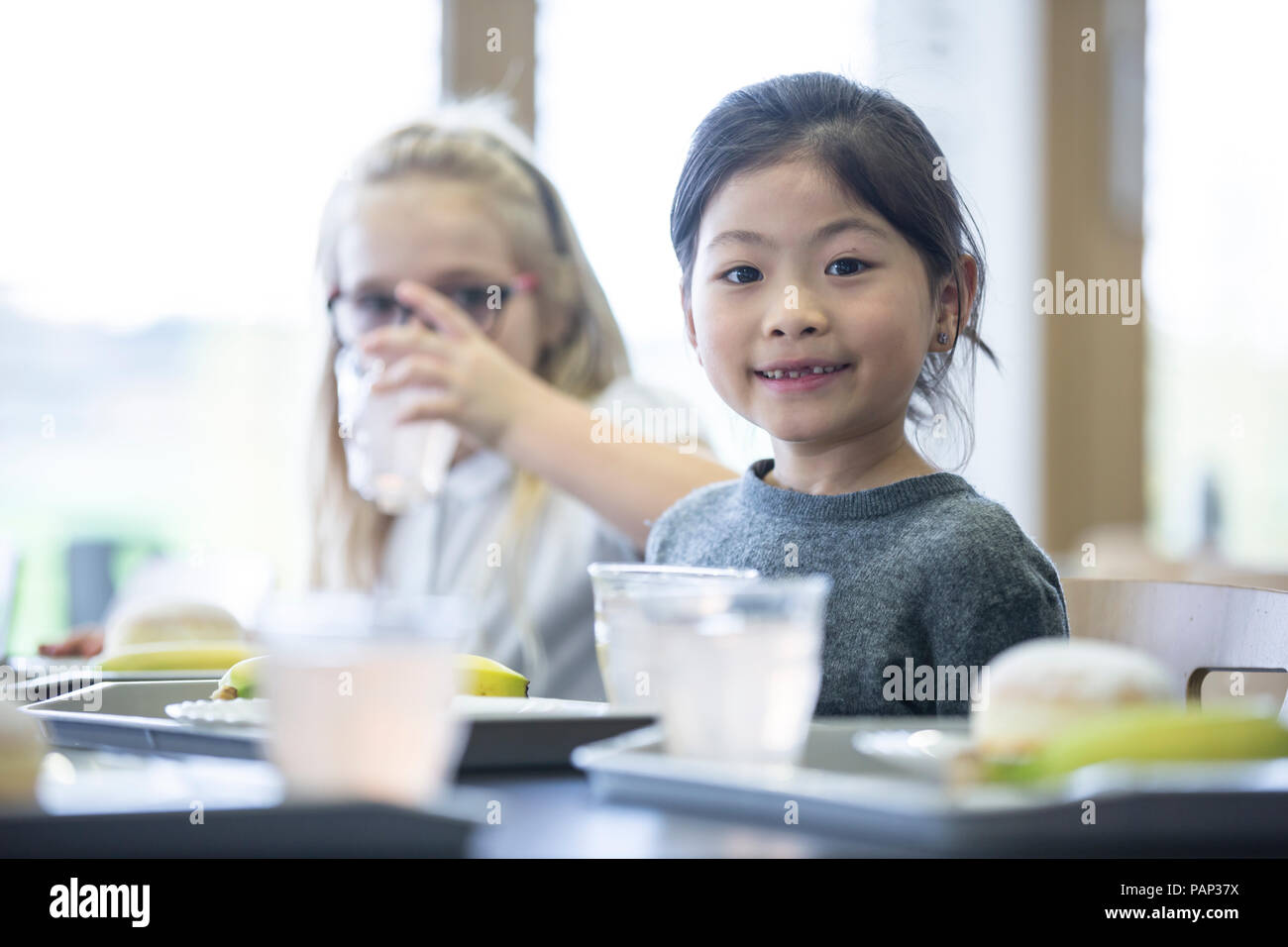 Ritratto di sorridere schoolgirl con un compagno di classe in mensa scolastica Foto Stock