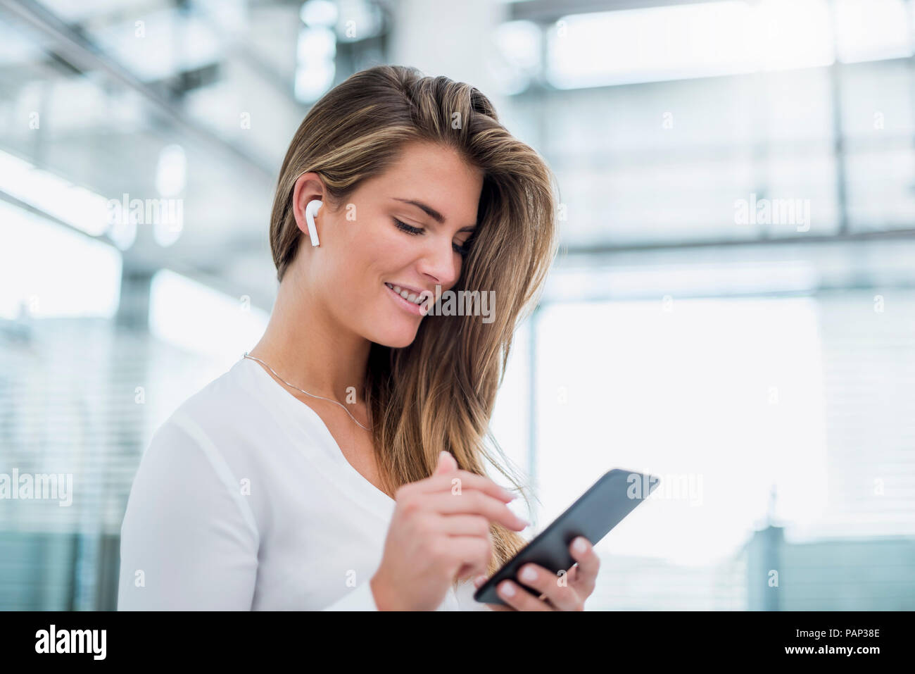 Sorridente giovane donna indossa in-ear telefono tramite telefono cellulare Foto Stock