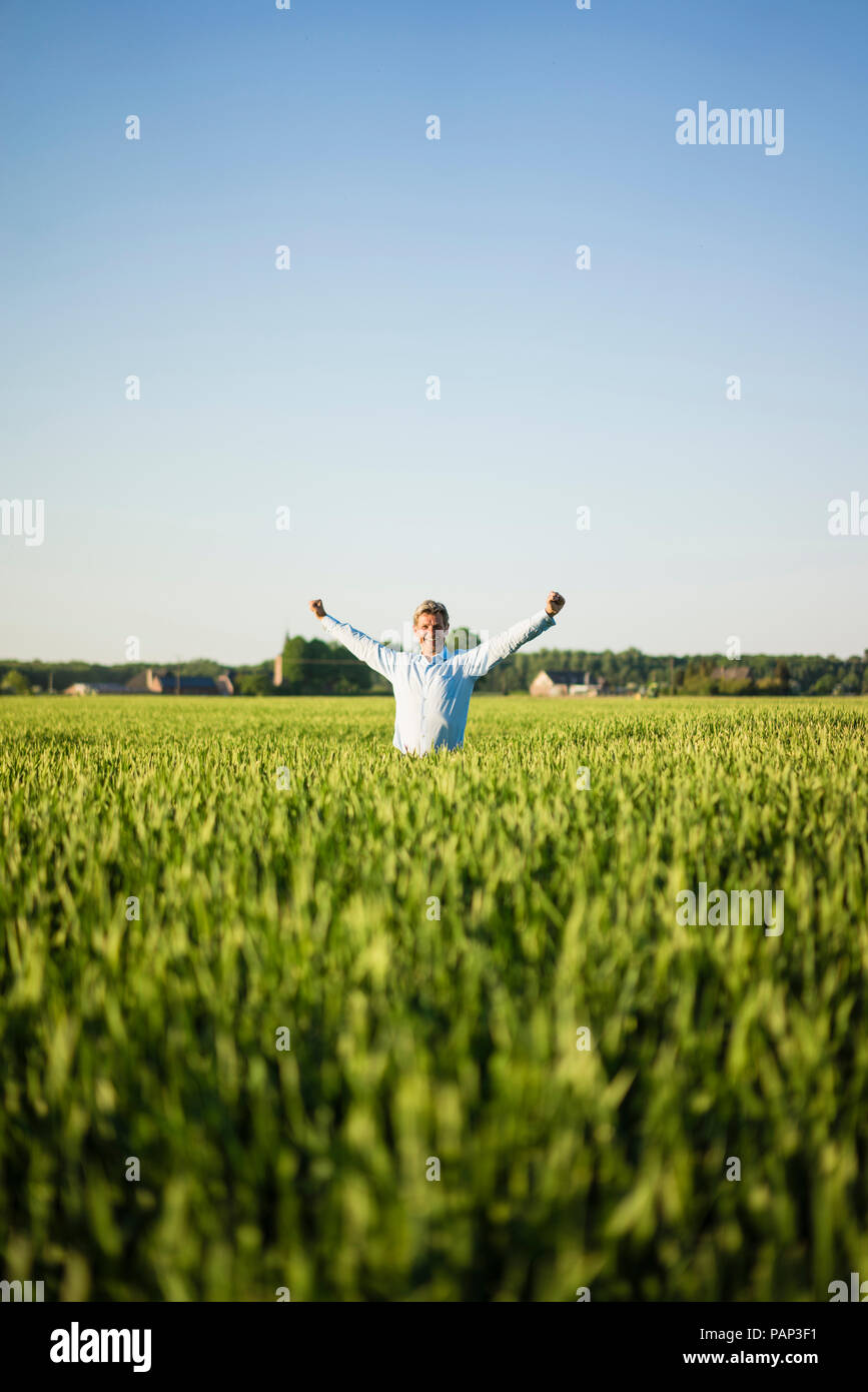 Imprenditore in piedi nel campo di grano, bracci sollevati Foto Stock
