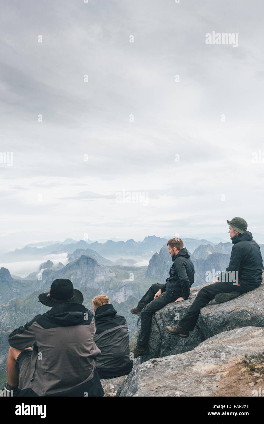 Norvegia Lofoten, Moskenesoy, giovani uomini seduti a Hermannsdalstinden, guardando sopra Kjerkefjord Foto Stock