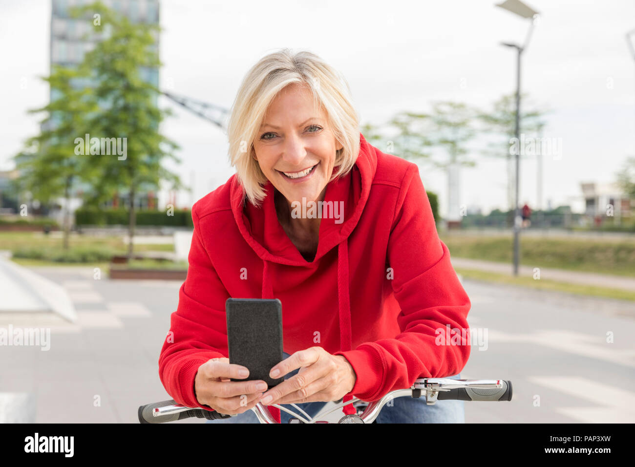 Ritratto di sorridente donna senior con city bike e il telefono cellulare Foto Stock