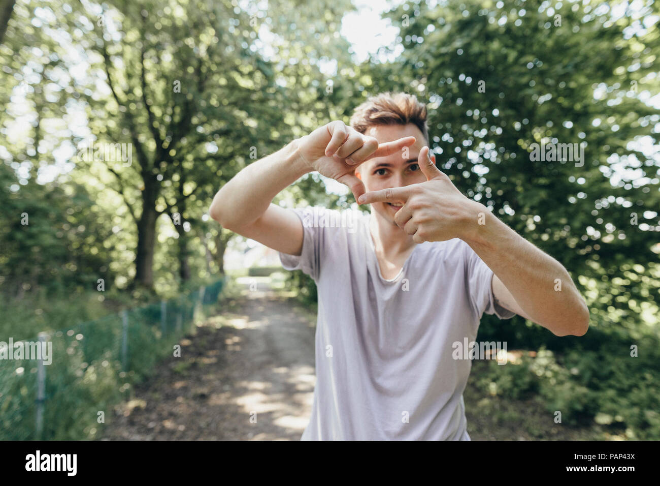 Giovane uomo che fa un dito telaio sul sentiero forestale Foto Stock