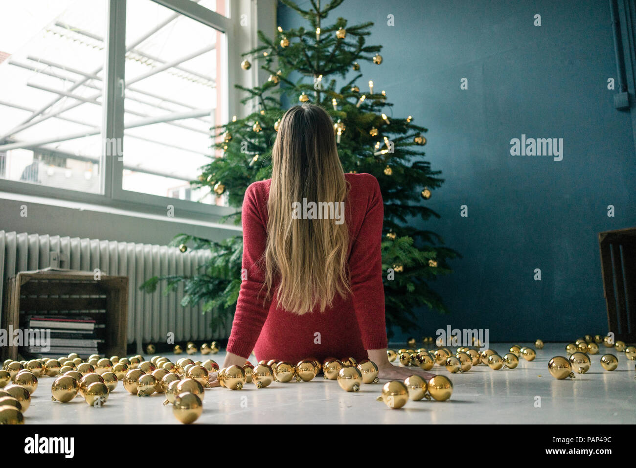 Vista posteriore della donna seduta sul pavimento con molti golden baubles di Natale guardando albero di Natale Foto Stock