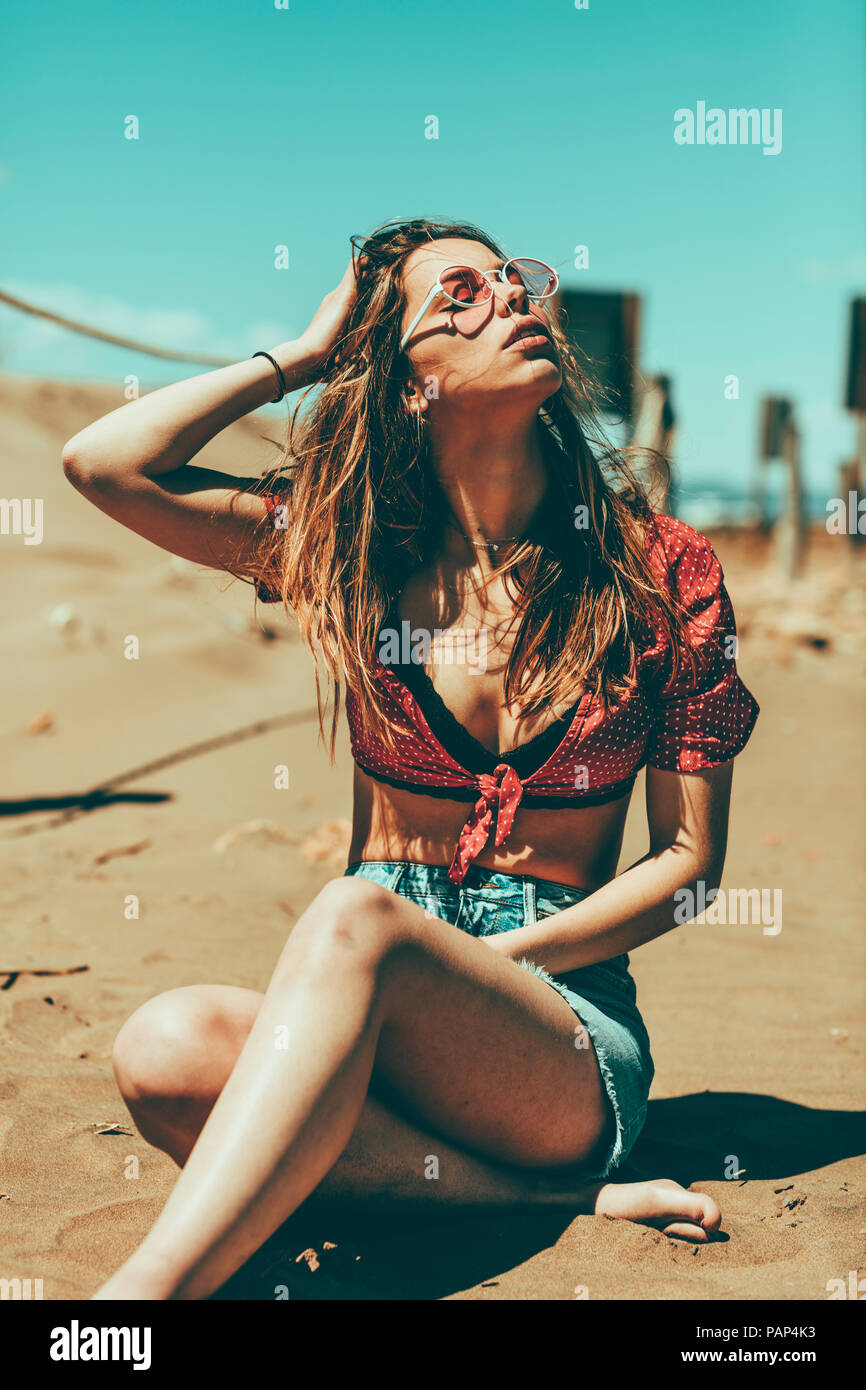 Giovane donna seduta sulla spiaggia sabbiosa Foto Stock