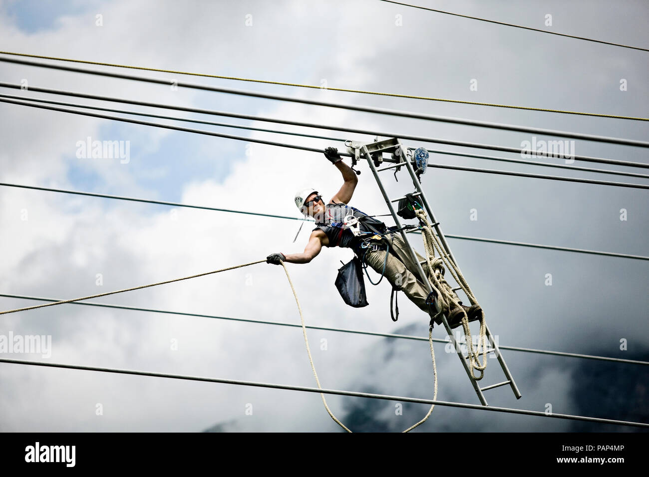 Montatore con scaletta, tirando lungo la linea elettrica ad alta tensione Foto Stock