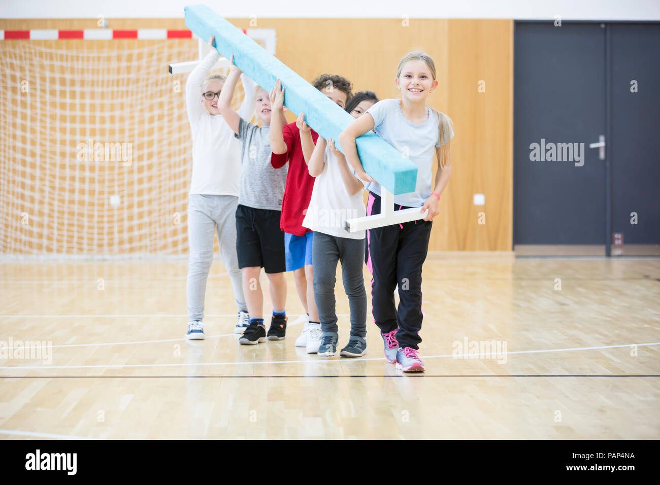 Gli alunni che trasportano il fascio di equilibrio nella palestra di classe Foto Stock