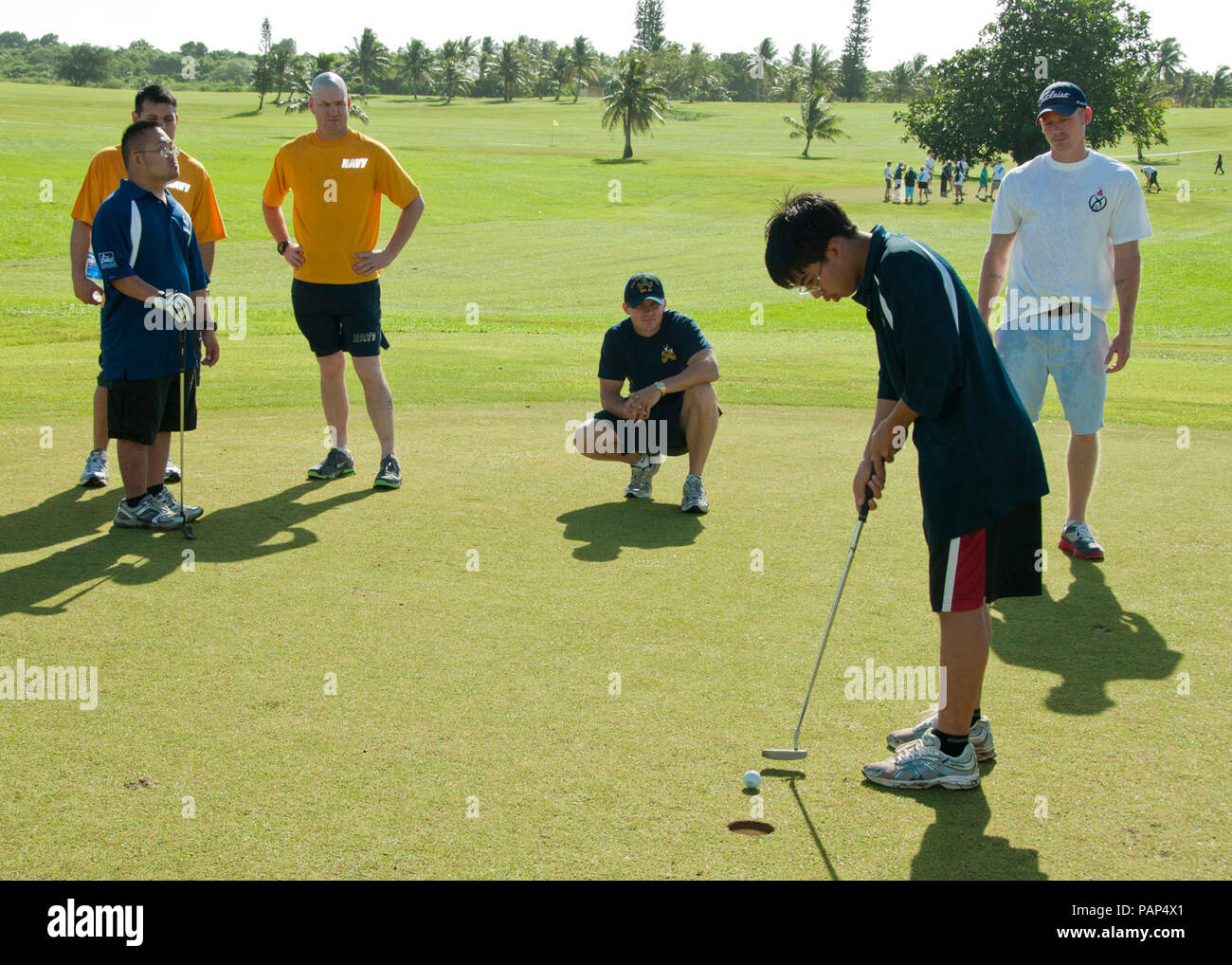 Un atleta degli Special Olympics putts una pallina da golf come volontari guardare durante la seconda edizione di Special Olympics di Guam golf mostra presso l'Admiral Nimitz golf Barrigada di, Guam, Dic 17, 2011. Stati Uniti I membri del servizio, insieme con i marinai dalla visita di missile destroyer USS John Paul Jones (DDG 53), volontariamente il loro tempo per garantire gli atleti hanno avuto un sicuro e divertente evento. Foto Stock