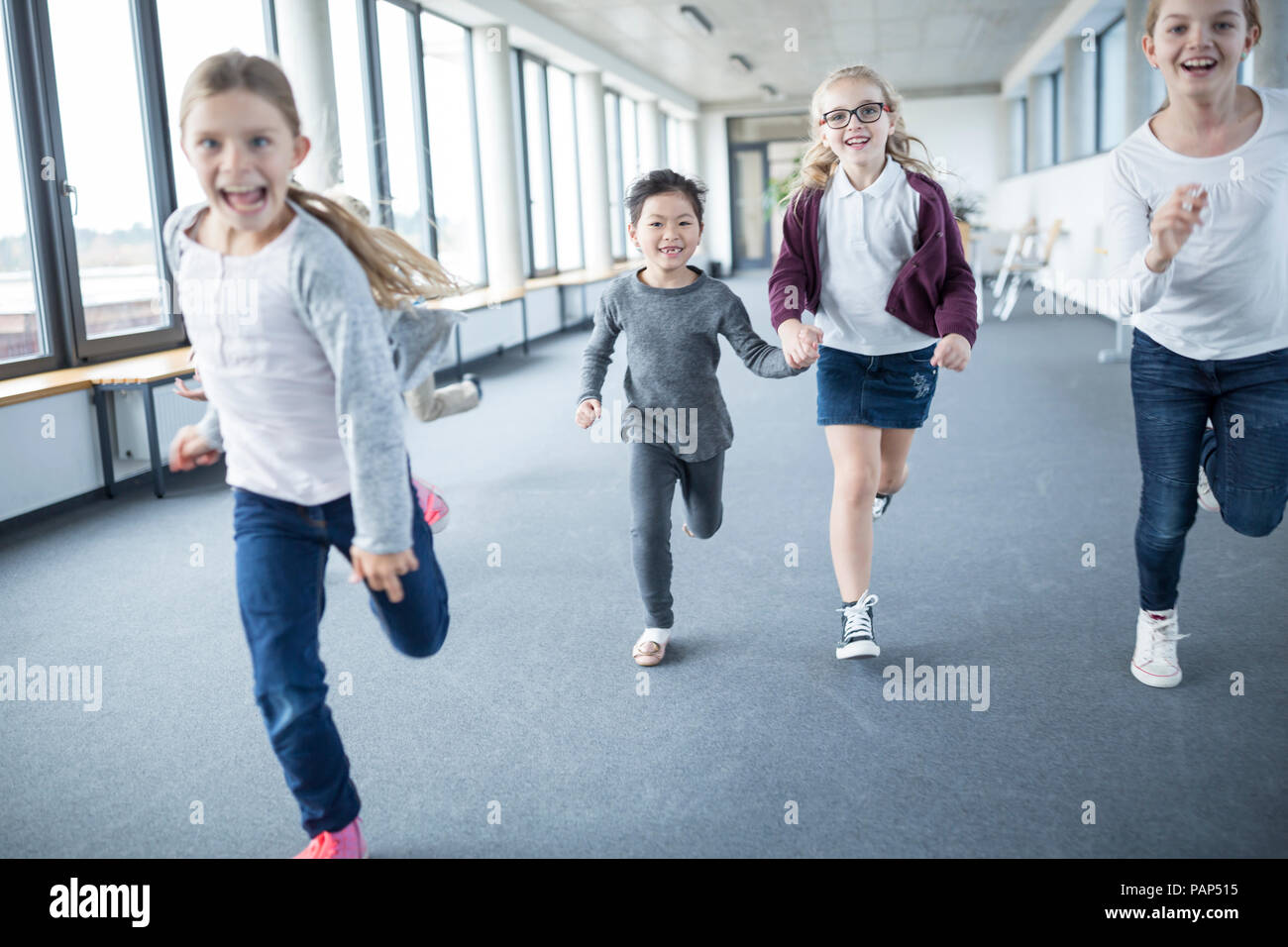 Emozionato studentesse correre verso il basso corridoio della scuola Foto Stock