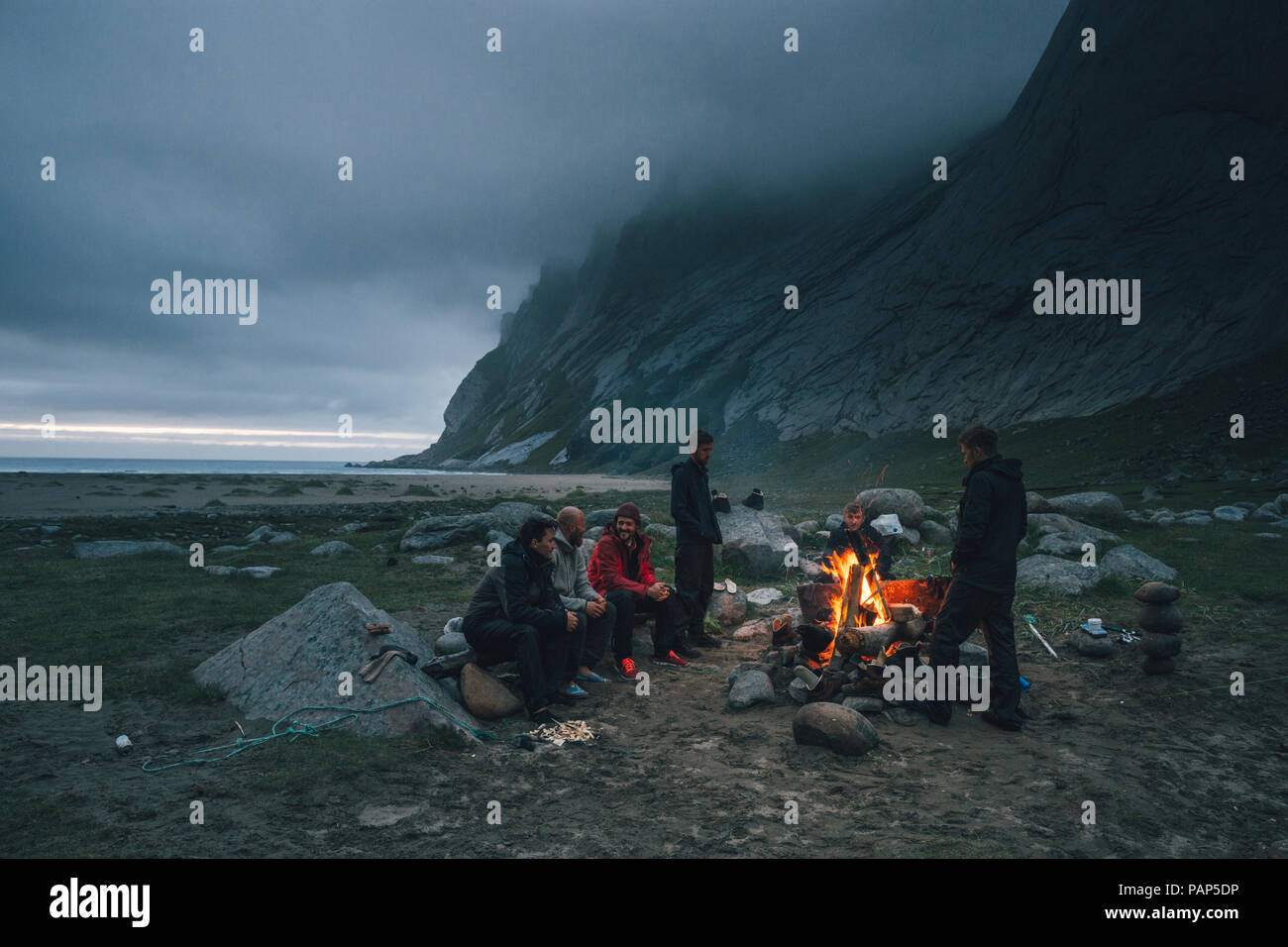 Norvegia Lofoten, Moskenesoy, un gruppo di giovani uomini seduti a un falò in spiaggia Bunes Foto Stock