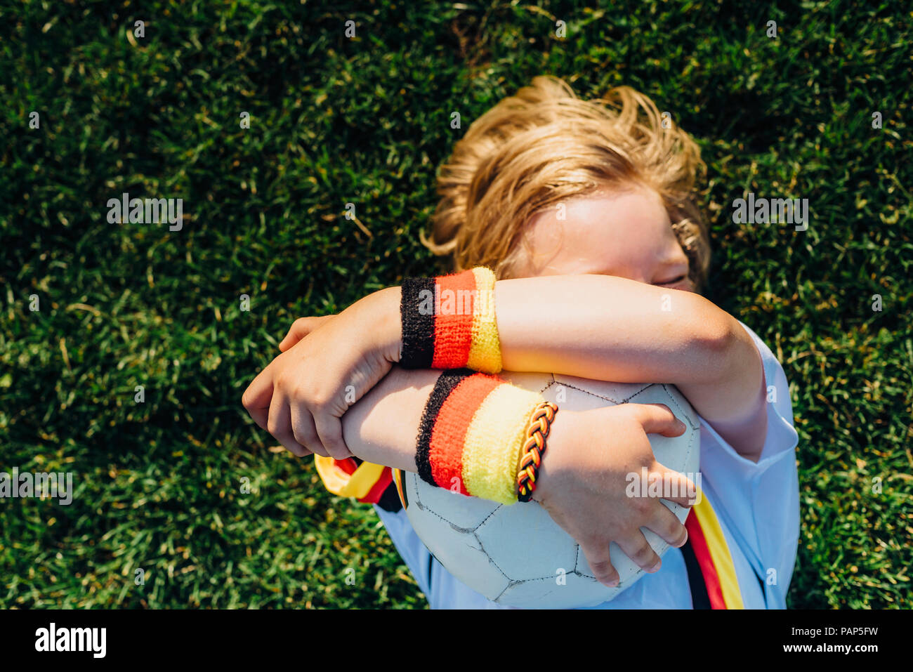 Ragazzo in calcio tedesco shirt giacente su erba, abbracciando la sfera Foto Stock