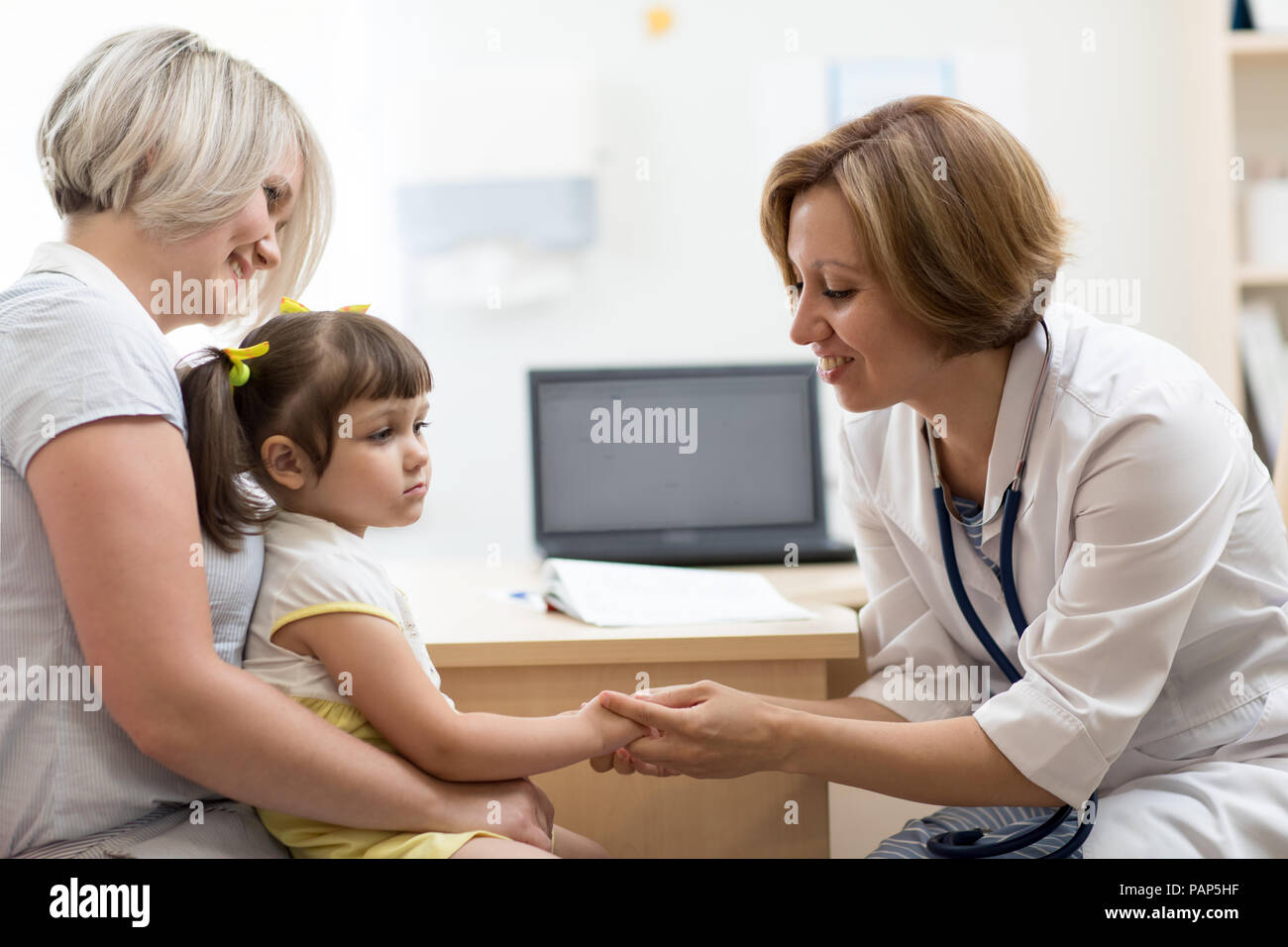 Medico pediatra azienda bambino la mano nelle sue mani. Piccola ragazza seduta alla madre di ginocchia Foto Stock