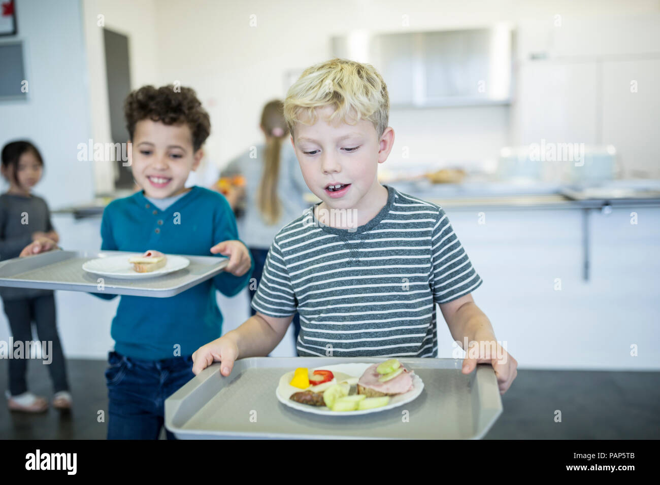Gli alunni che porta i vassoi in mensa scolastica Foto Stock