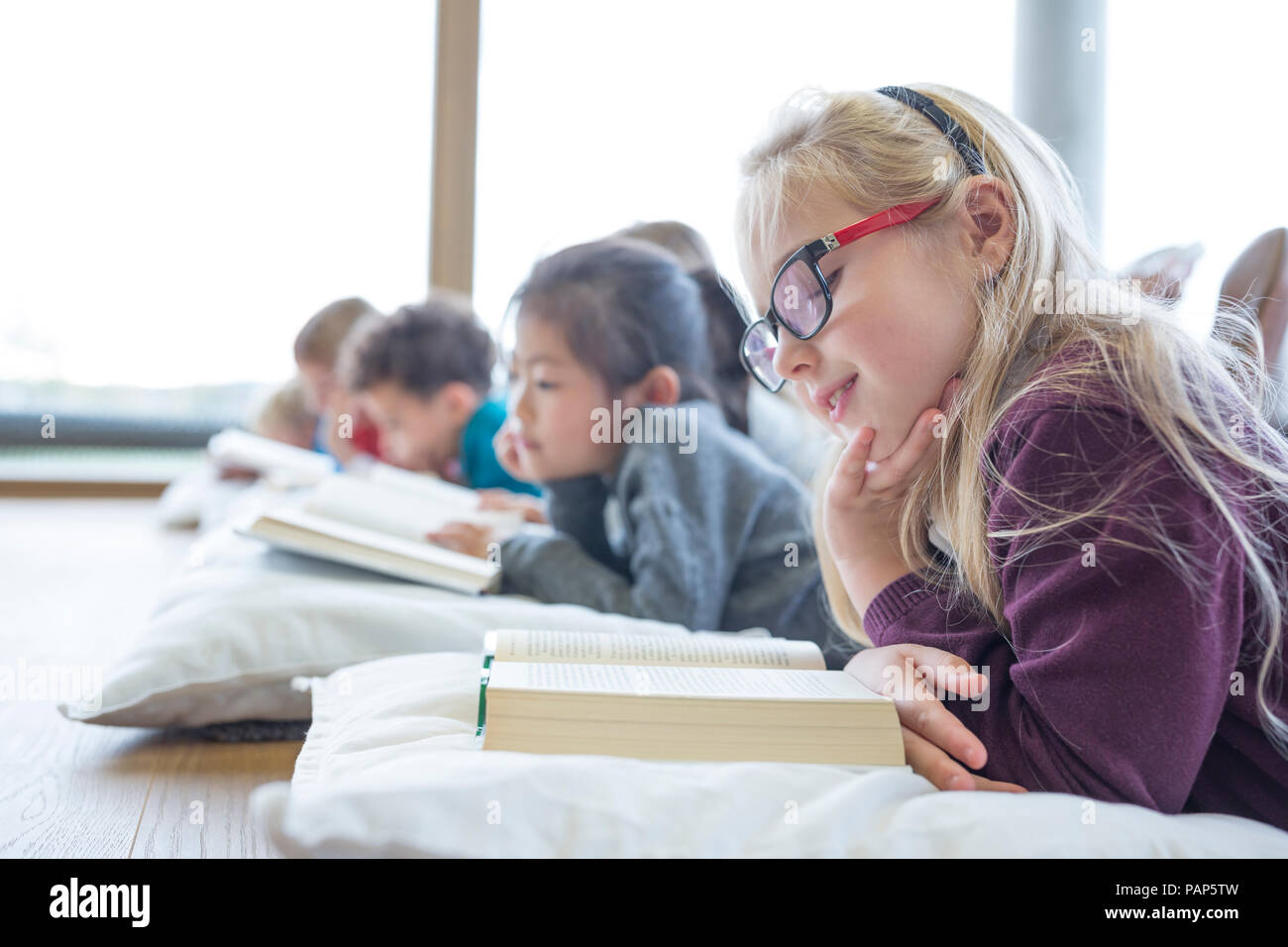 Gli alunni sdraiato sul pavimento la lettura di libri di scuola sala pausa Foto Stock