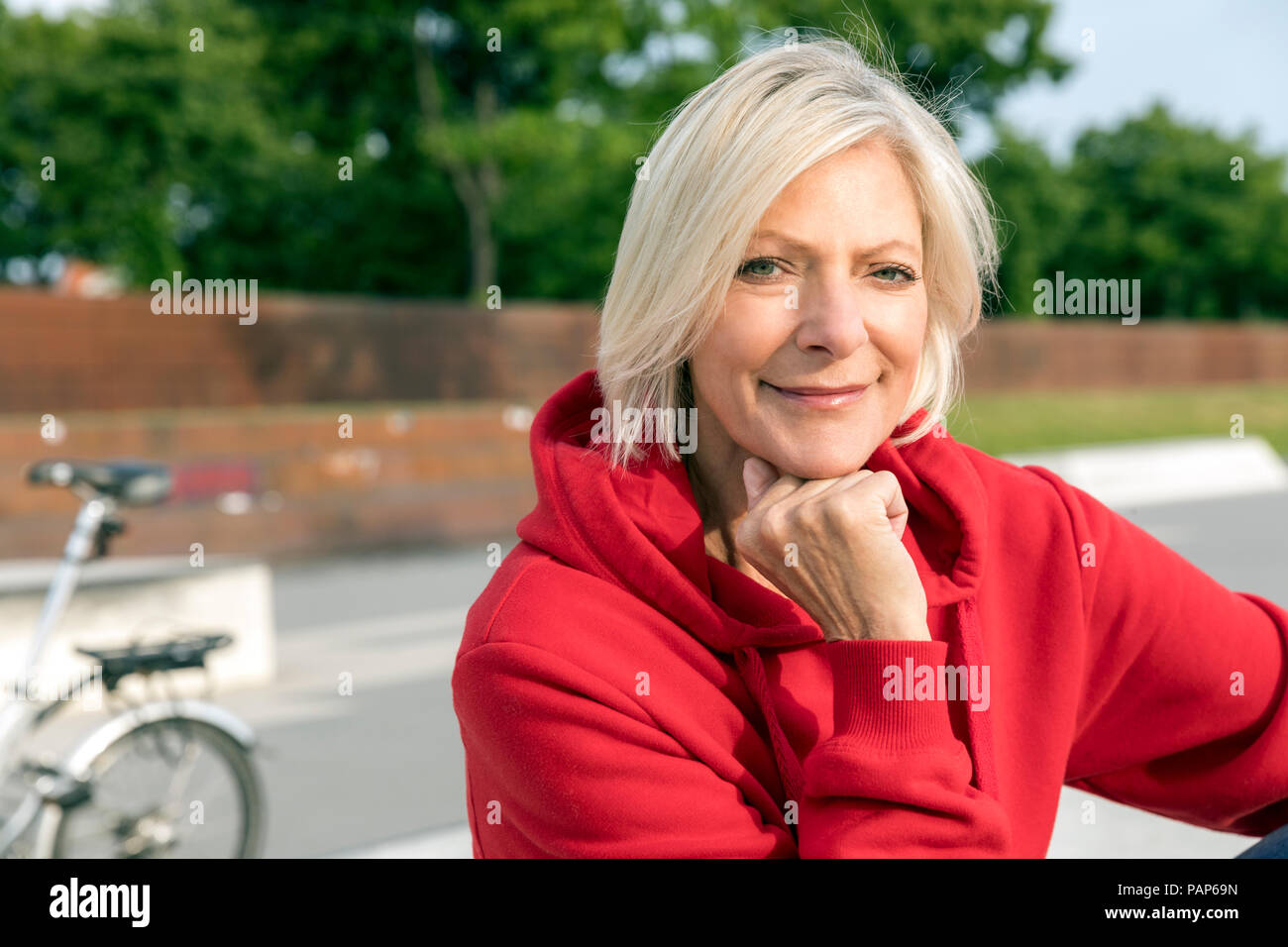 Ritratto di sorridere senior donna che indossa felpa con cappuccio rosso all'aperto Foto Stock