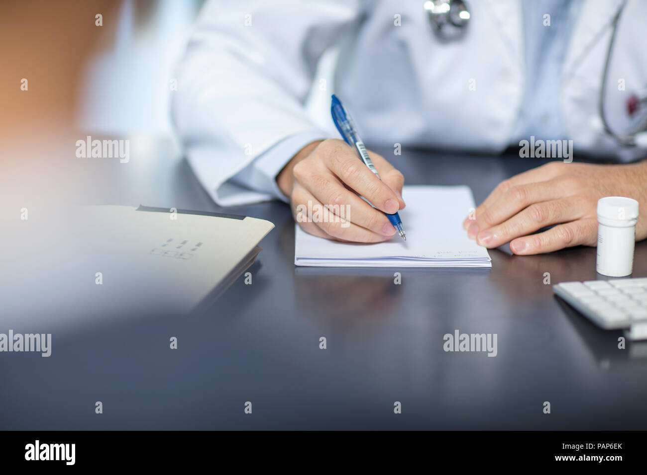 Medico seduto alla sua scrivania prendendo appunti Foto Stock