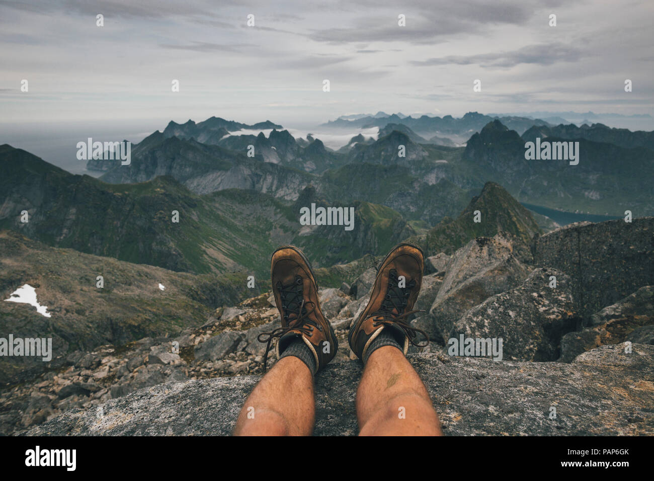 Norvegia Lofoten, Moskenesoy, giovane uomo seduto al Hermannsdalstinden, guardando sopra Kjerkefjord Foto Stock