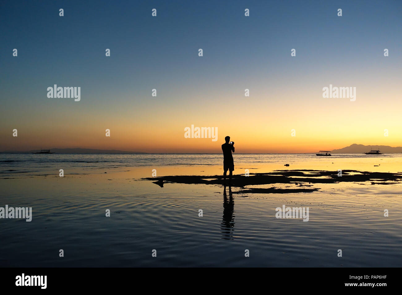 Uomo turistica per scattare delle foto su un isola rocciosa spiaggia a bassa marea - Alona, Bohol Foto Stock