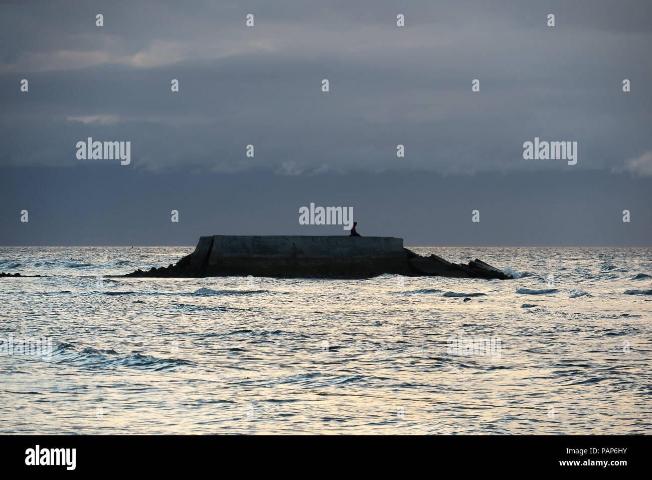 Un uomo in ginocchio e meditando o pregando in un'isola di rock in mare - Bohol, Filippine Foto Stock