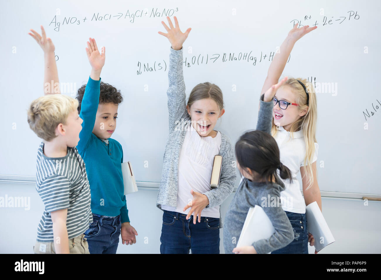 Felice gli alunni ad alzare la mano alla lavagna con formule in classe Foto Stock
