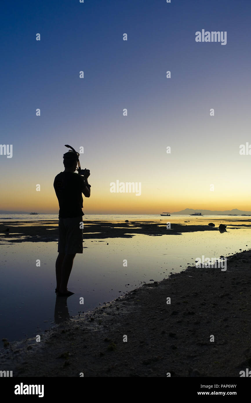 Silhouette di uomo con maschera Snorkel prendendo le foto del tramonto sulla spiaggia con la bassa marea - Panglao, Filippine Foto Stock
