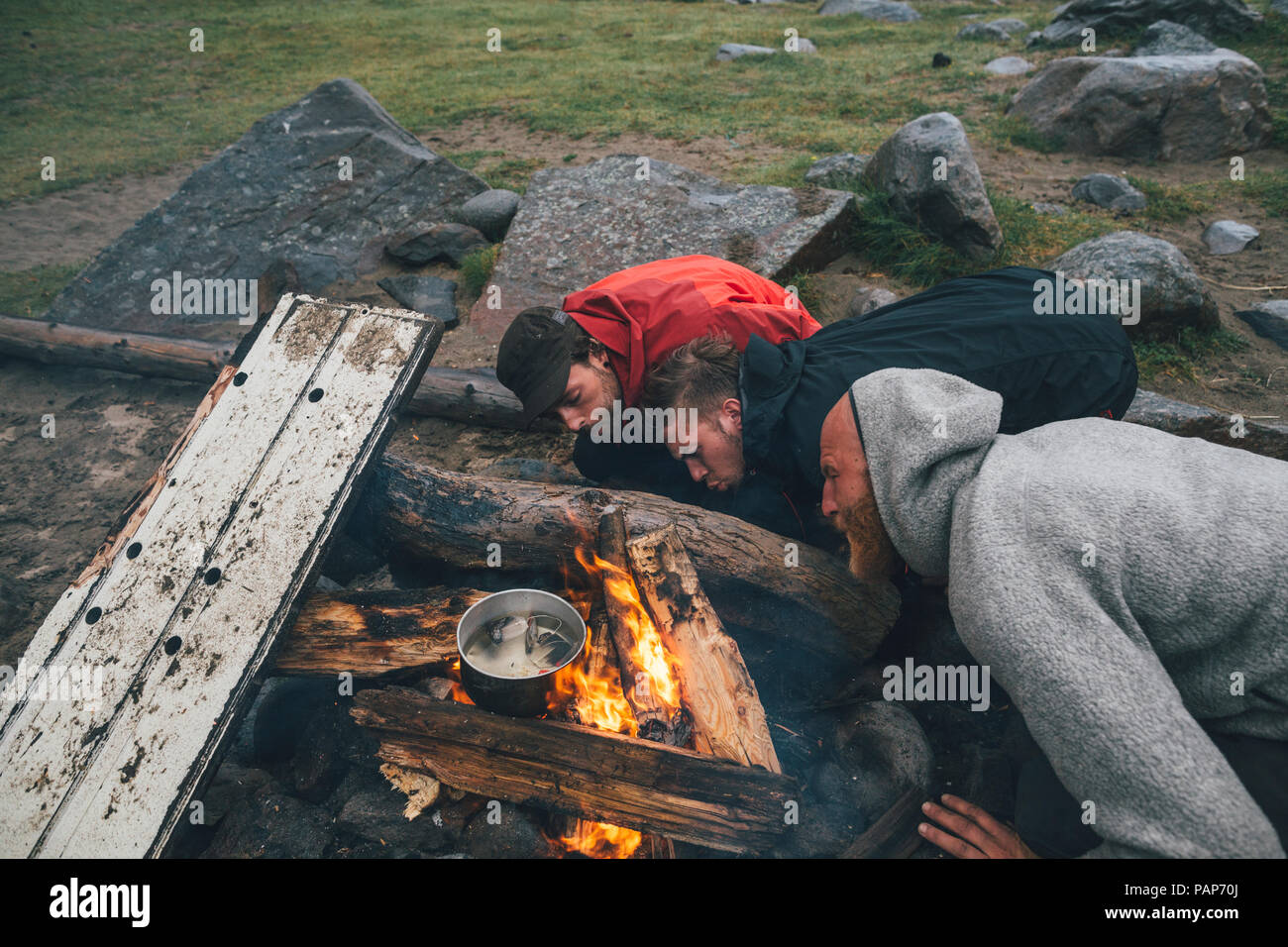 Norvegia Lofoten, Moskenesoy, tre uomini fanning le fiamme di un fuoco di campo a Bunes Beach Foto Stock