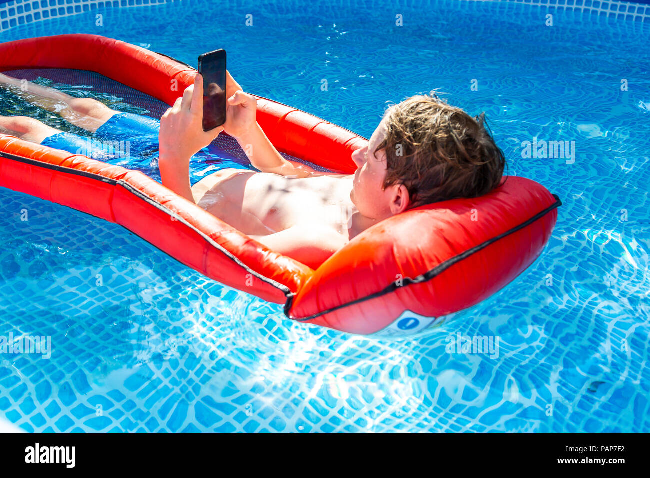 Ragazzo galleggiante sull'acqua in piscina utilizza lo smartphone Foto Stock