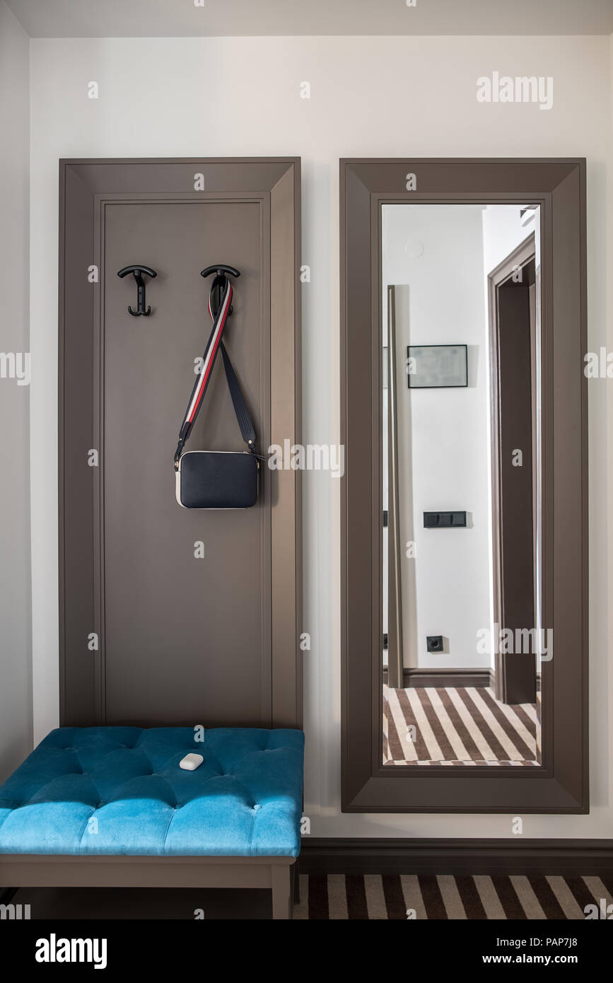 Corridoio in una stanza di un hotel con la luce pareti e un pavimento striato. Non vi è un supporto blu, specchio di lunghezza completa, appendiabiti con appeso un borsa a tracolla. In verticale Foto Stock