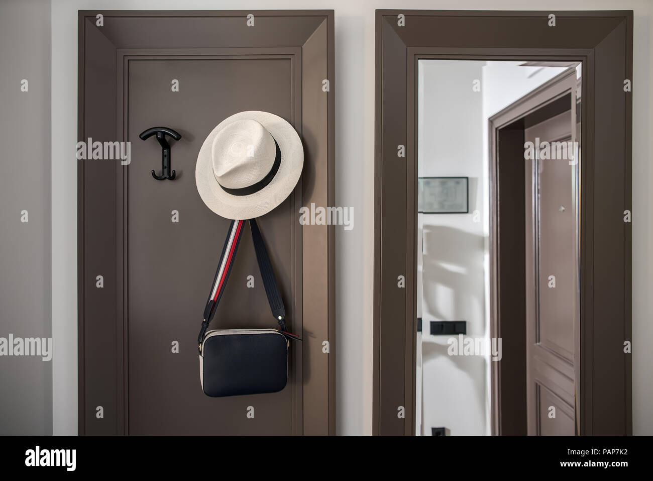 Corridoio contemporaneo in una camera di hotel con pareti chiare. Vi è uno specchio di lunghezza completa, appendiabiti con appeso un borsa a tracolla e un cappello. Orizzontale. Foto Stock