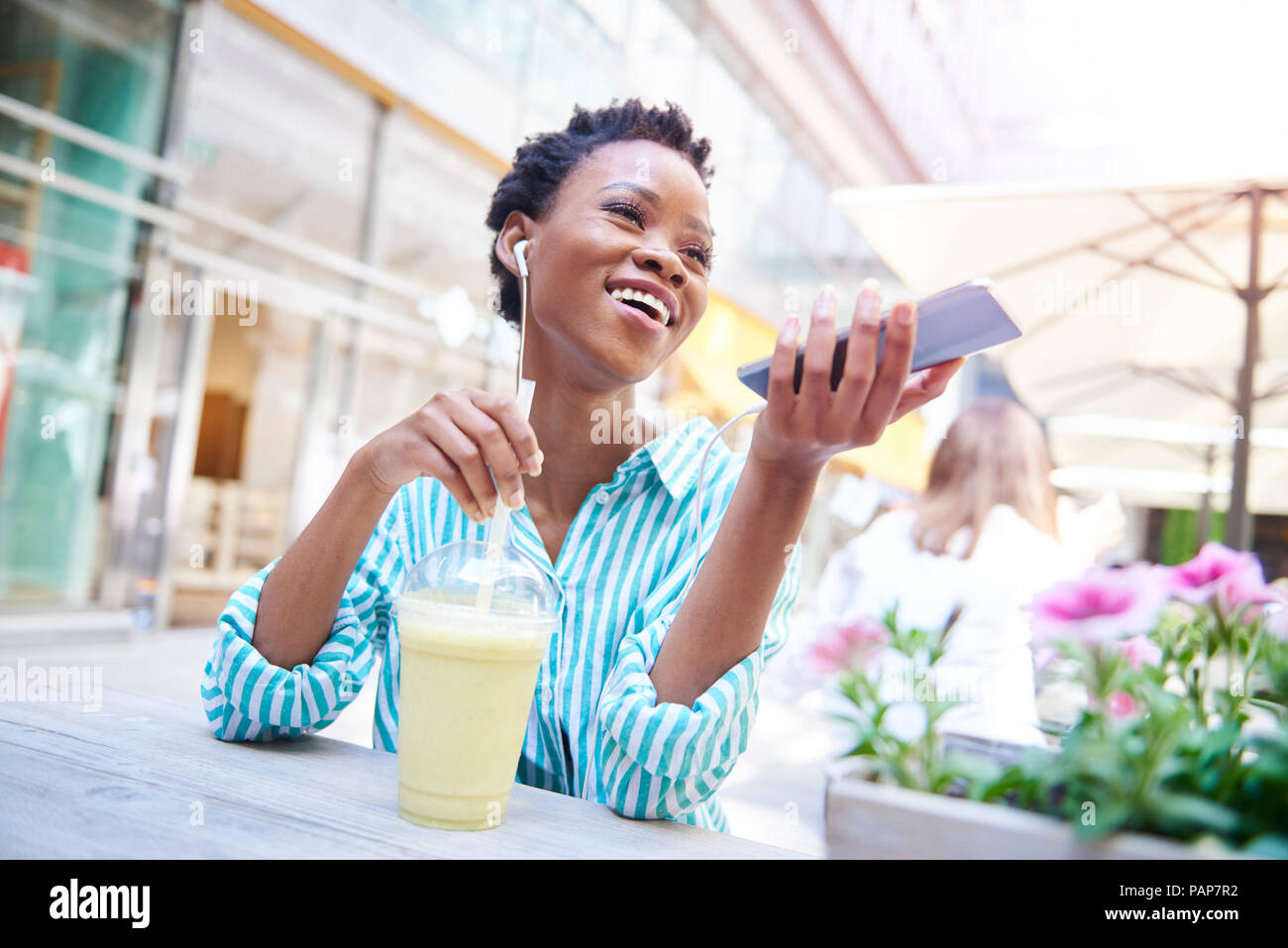 Ritratto di donna ridere sul telefono cellulare al cafe' sul marciapiede Foto Stock