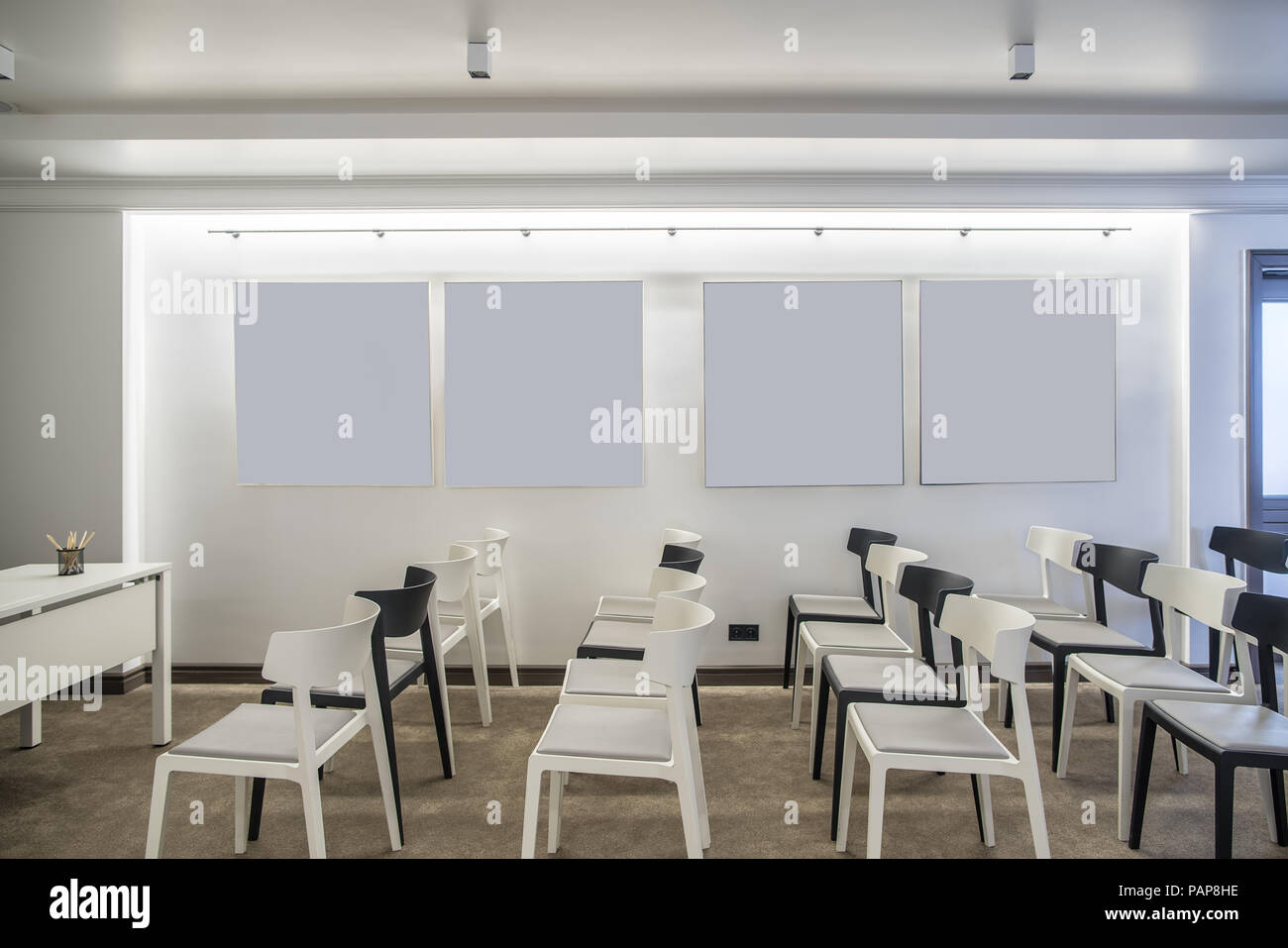 Contemporanea sala conferenza con pareti bianche. Ci sono molti chiari e scuri di sedie, tavolo, spie luminose, porta. Orizzontale. Foto Stock