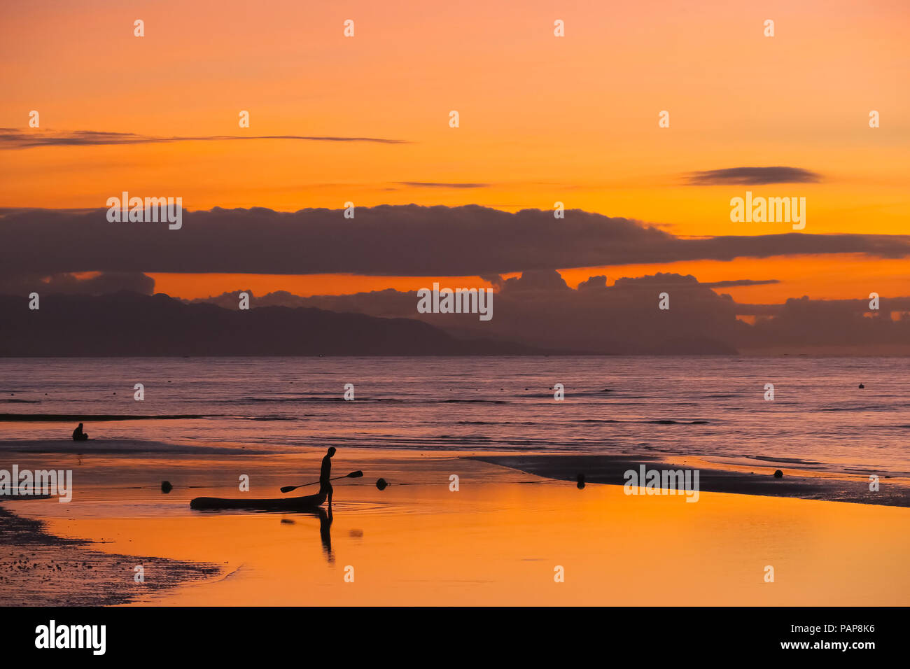 Silhouette di uomo sulla spiaggia trascinando un kayak in mare durante un nuvoloso, isola di Orange Sunrise in Panglao, Filippine Foto Stock