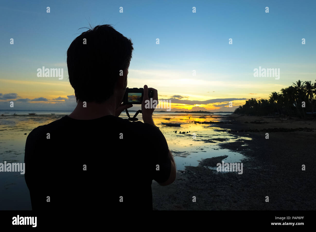 Fotografo uomo con fotocamera, tiro verso il tramonto su una spiaggia durante la vacanza isola - Boracay, Aklan - Filippine Foto Stock
