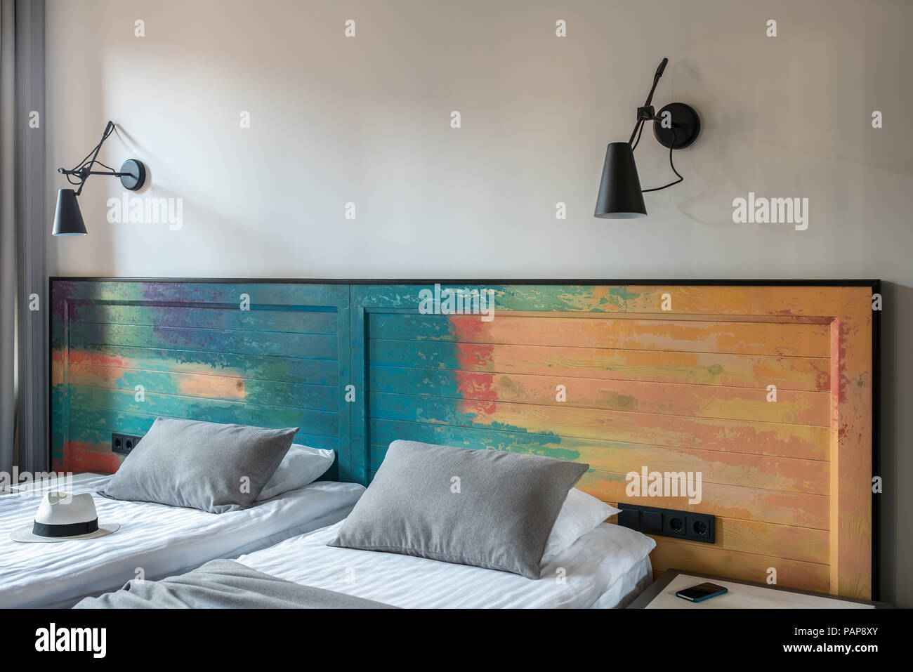 Bella camera in un albergo con pareti chiare. Ci sono due letti singoli con un coloratissimo testata in legno nero, lampade a parete, tenda, comodino con un smartpho Foto Stock