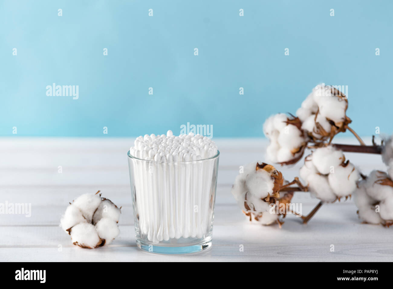 Tamponi di cotone in chiaro il vasetto di vetro nel bagno impostazione con un cotone fiori pastello su sfondo blu. Spazio di copia Foto Stock