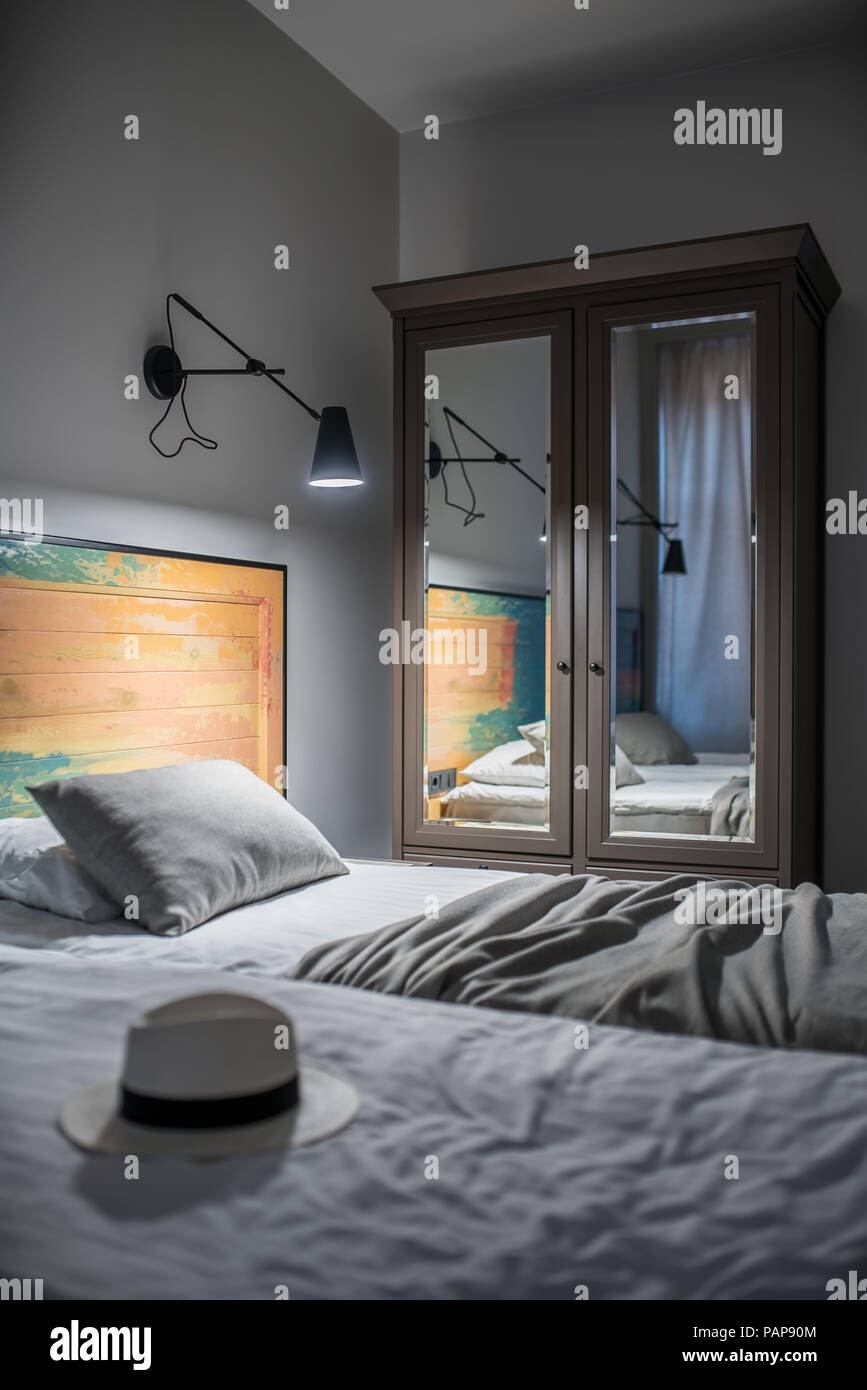 Camera luminosa in un hotel con pareti chiare. Ci sono due letti singoli con un coloratissimo testata in legno nero, lampade a parete, finestra con tende, nightstan Foto Stock