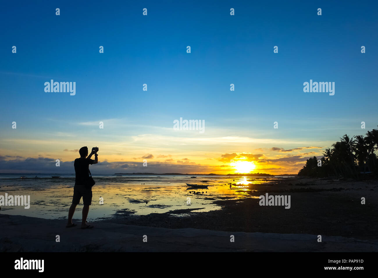 Fotografo di viaggio uomo scattare le foto di una bellissima isola blu tramonto su una spiaggia rocciosa - Boracay, Aklan - Filippine Foto Stock
