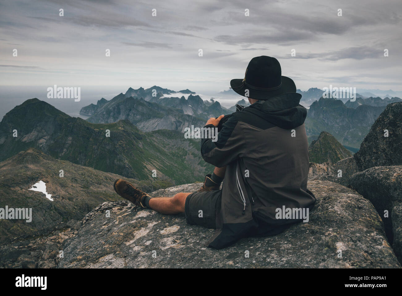 Norvegia Lofoten, Moskenesoy, giovane uomo seduto al Hermannsdalstinden, guardando sopra Kjerkefjord Foto Stock
