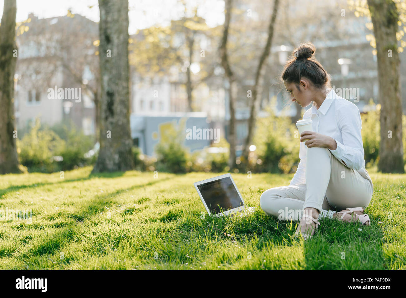 Giovane imprenditrice prendendo break, utilizzando laptop, seduta in erba e di bere il caffè Foto Stock