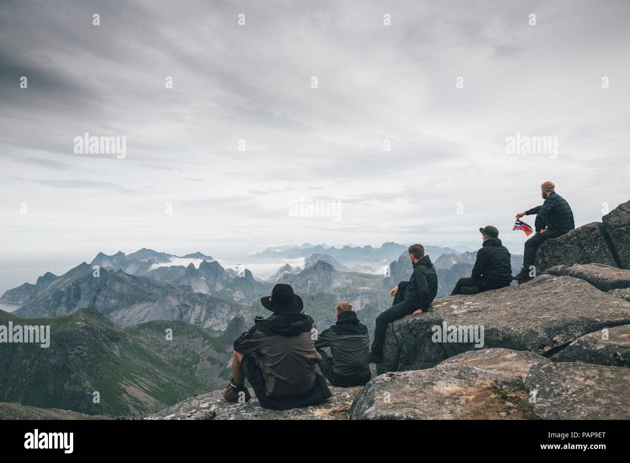 Norvegia Lofoten, Moskenesoy, giovani uomini seduti a Hermannsdalstinden, guardando sopra Kjerkefjord Foto Stock