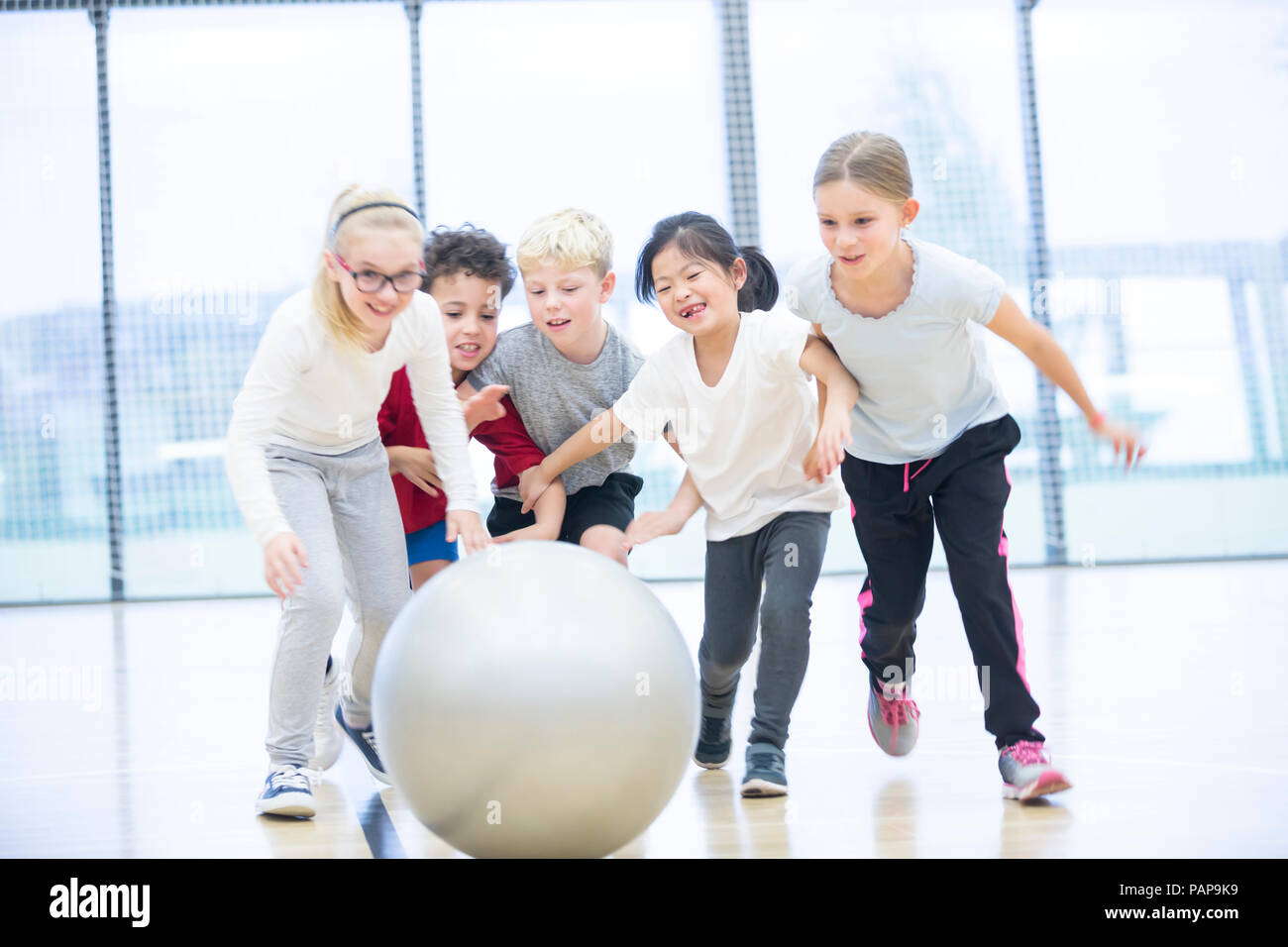 Felice gli alunni a giocare con palla in palestra classe Foto Stock