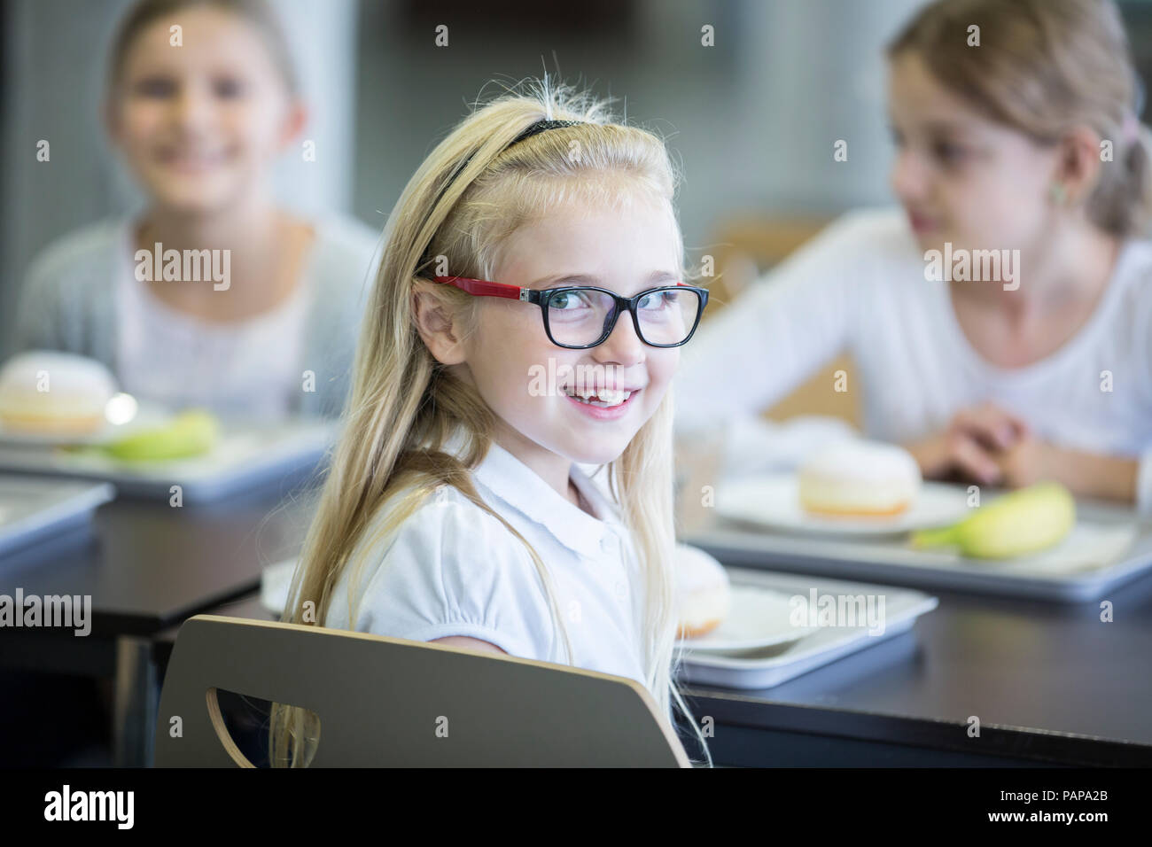 Ritratto di sorridere schoolgirl con i compagni di classe in mensa scolastica Foto Stock