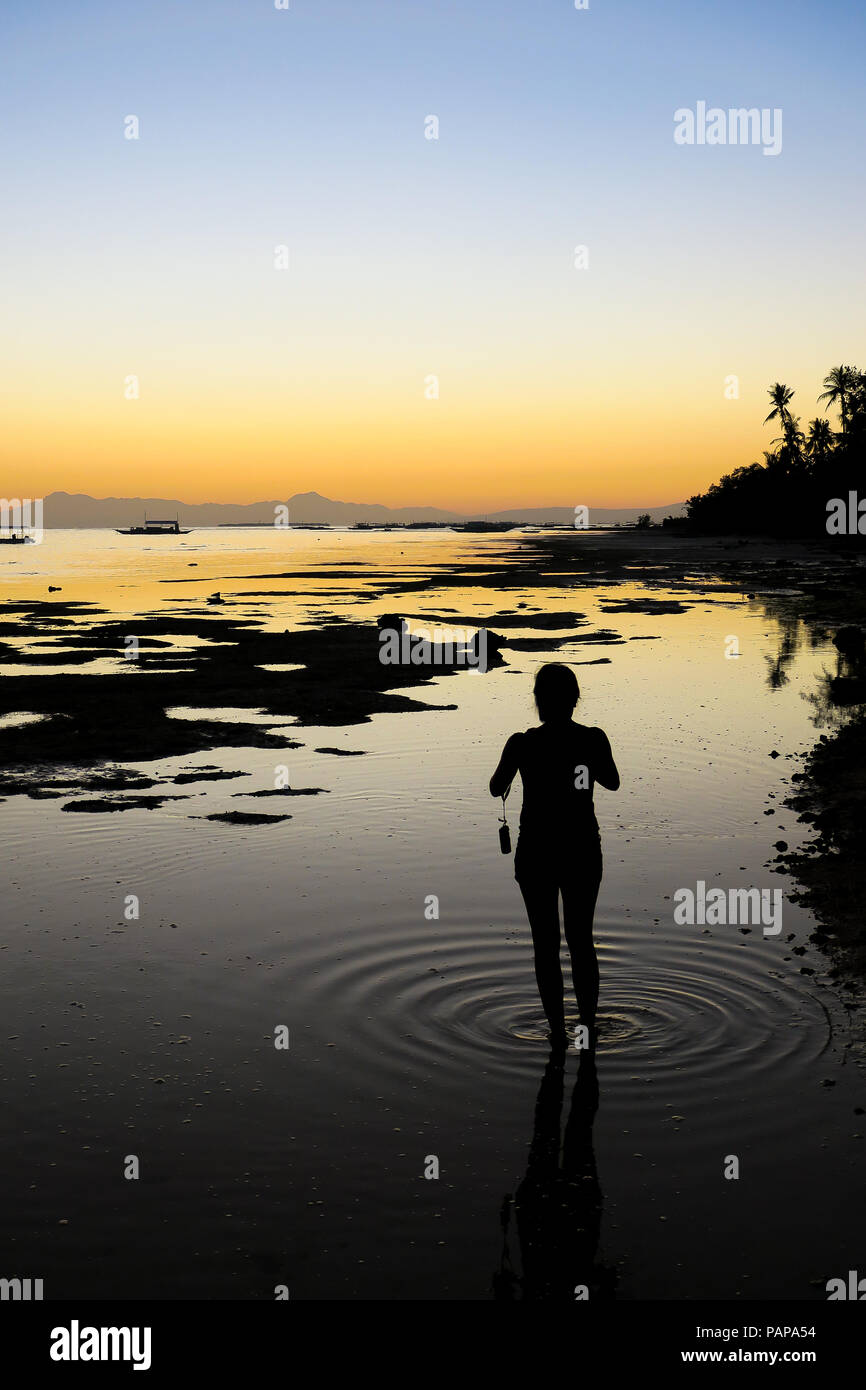 Donna in piedi in mare poco profondo e acqua a bassa marea, scattare foto con increspature ai suoi piedi - - Alona Beach, Bohol - Filippine Foto Stock