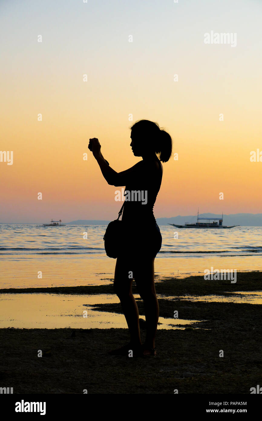 Profilo di Silhouette di una giovane donna di scattare foto durante una spiaggia al tramonto - Alona Beach, Bohol - Filippine Foto Stock