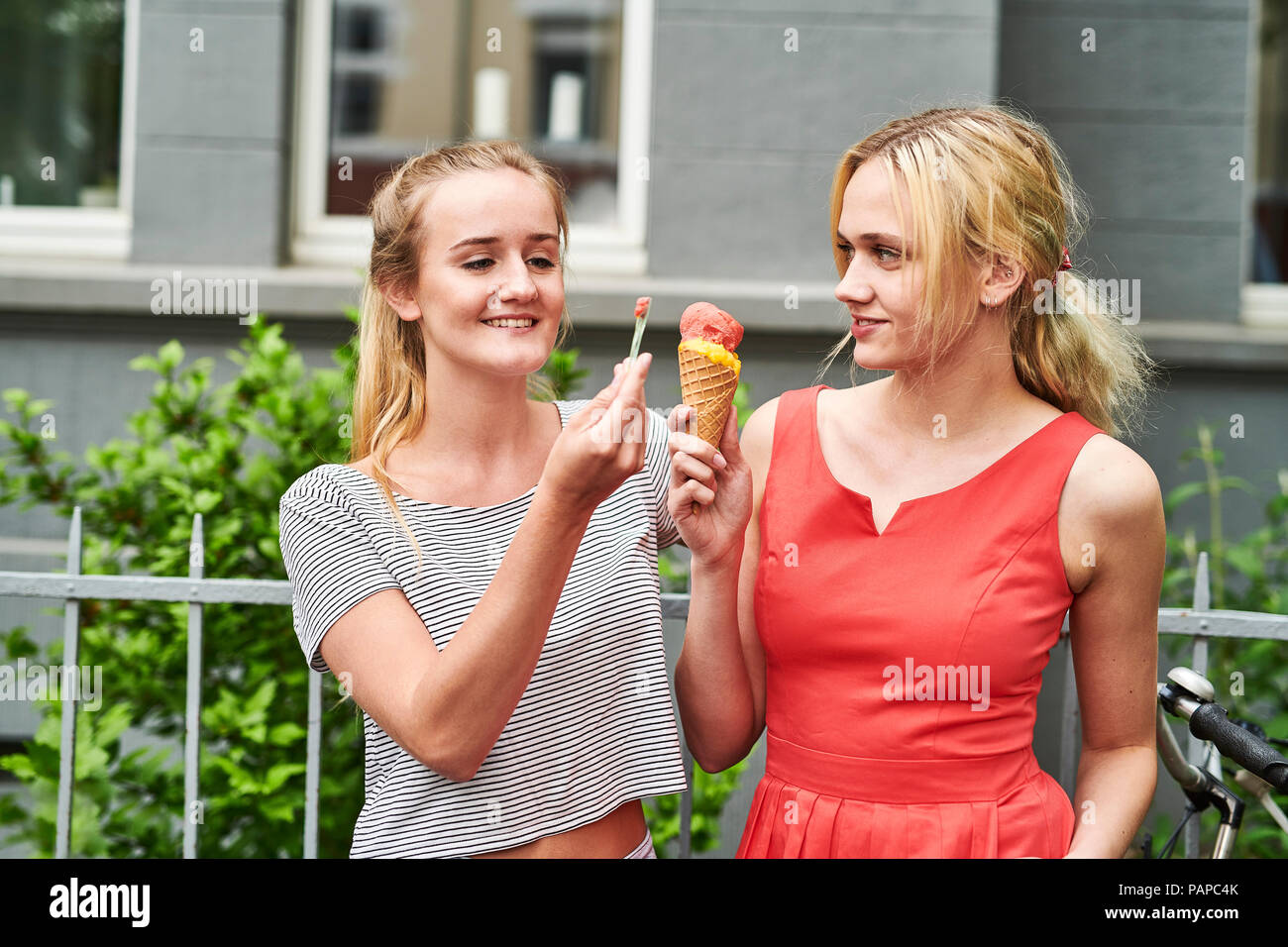 Due giovani donne che condividono un cono gelato nella città Foto Stock