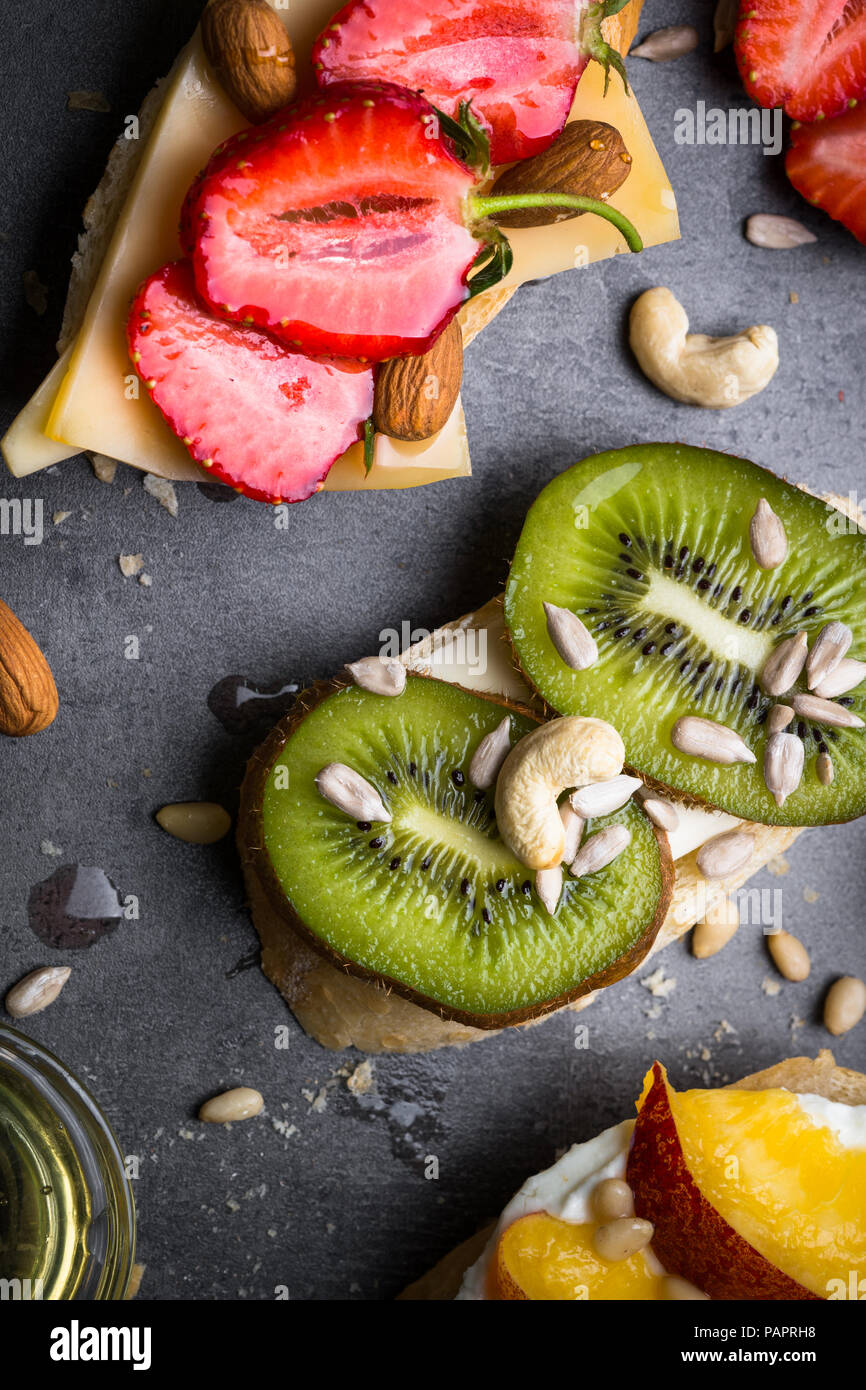 Fresca frutta dolci panini. Pesche Fragole e kiwi panini con noci e miele sulla tavola nera. Vista superiore vicino. Snack sani. Foto Stock
